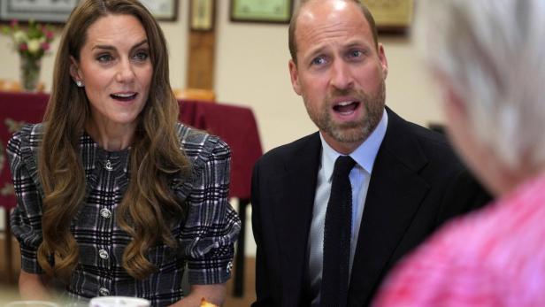 Kate und William sitzen an einem Tisch und unterhalten sich mit einer Person.