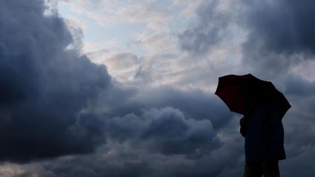 Eine Person mit einem Regenschirm vor einem dunklen, bewölkten Himmel.