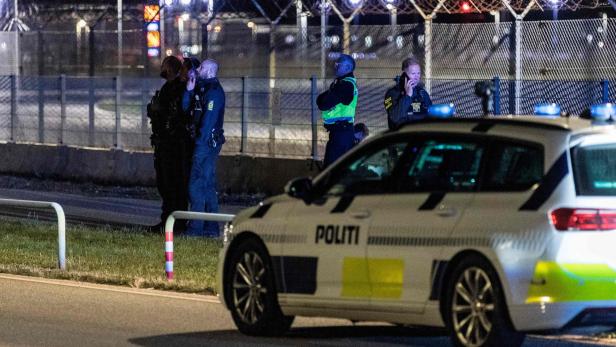 Bei Nacht stehen Polizisten vor einem Zaun mit Stacheldraht, ein Polizeiauto im Vordergrund.