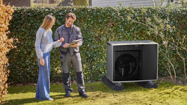 Wärmepumpe in einem Garten mit glücklicher Hausbesitzerin und glücklichem Installateur daneben.