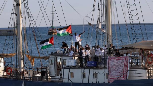 Mehrere Menschen stehen auf einem Segelschiff mit palästinensischen Flaggen, das auf dem Meer fährt.