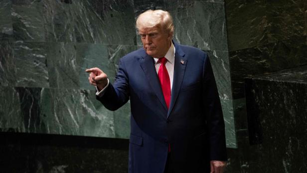 Donald Trump im dunklen Anzug mit roter Krawatte zeigt mit dem Finger nach links.