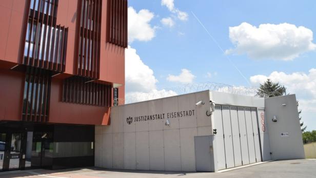 Modernes Gebäude mit roten Fassadenelementen und einem gesicherten Bereich mit Stacheldraht und Überwachungskameras.