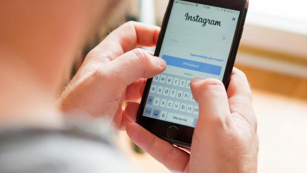 Ein junger Mann, der auf sein Handy Instagram geöffnet hat.