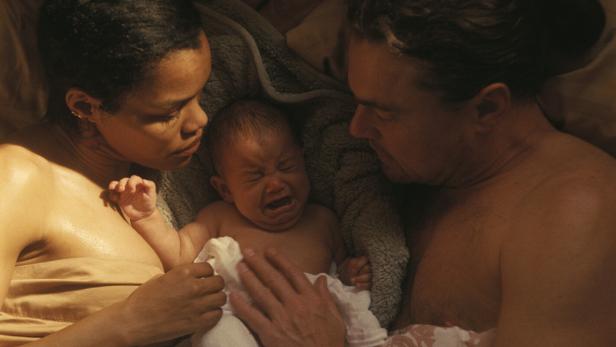 Ein Mann und eine Frau liegen im Bett, zwischen ihnen ein Baby.