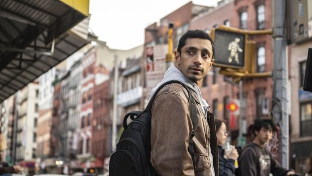 Ein Mann steht mit einem Rucksack in der Stadt vor einer Verkehrsampel.