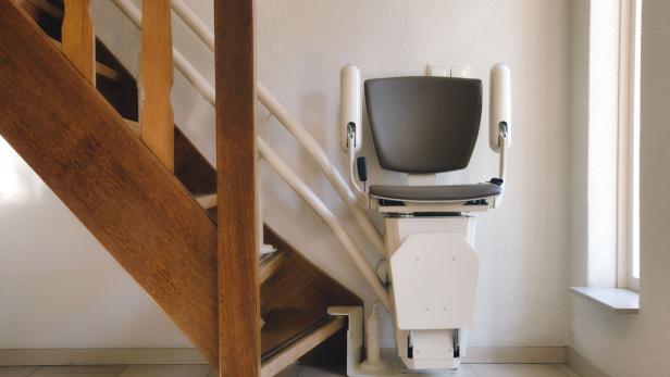 Treppenlift am Fuße einer hölzernen Stiege in einem Haus.