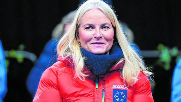 Mette-Marit in roter Jacke mit dem Logo "Trondheim 2025" blickt in die Kamera.