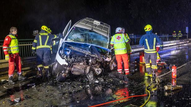 Mehrere Menschen in Einsatzuniformen stehen nachts auf einer Straße rund um ein desolates Fahrzeug.