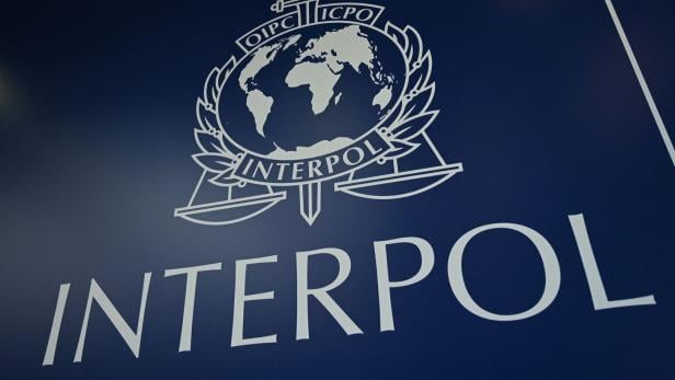 Das Interpol-Logo mit einer Weltkarte, einem Schwert, Lorbeerzweigen und einer Waage auf blauem Hintergrund.