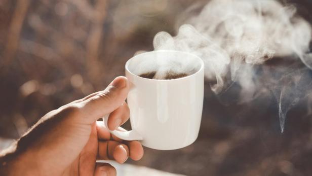  Mann hält dampfende Kaffeetasse hoch