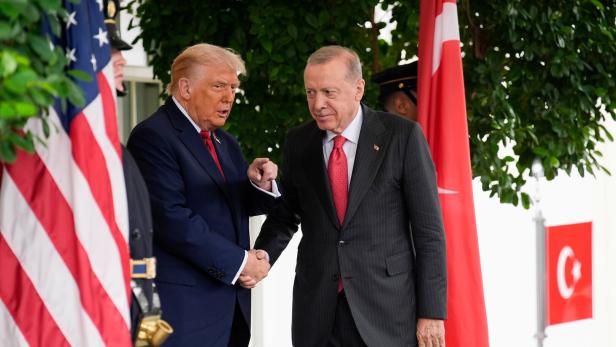 Donald Trump und Recep Tayyip Erdoğan geben sich vor US- und türkischen Flaggen die Hand.
