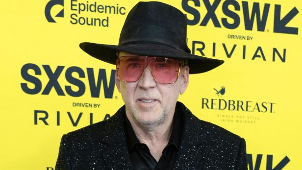 Nicolas Cage mit Hut und rosafarbener Brille vor gelbem SXSW-Hintergrund.