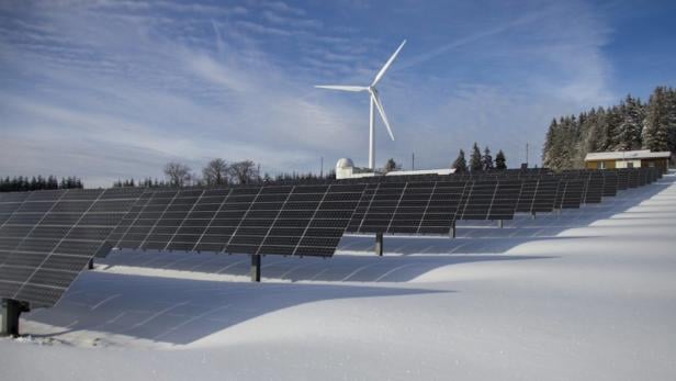 Solarpanels und Windräder stehen im Schnee, umweltfreundliche Energieerzeugung in winterlicher Landschaft.