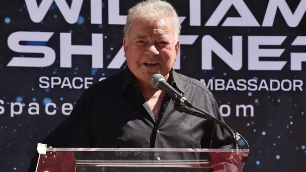 William Shatner spricht am Rednerpult vor einem Hintergrund mit seinem Namen.