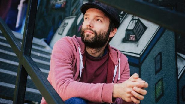 Ein Mann mit Bart und Schirmmütze - Marc-Uwe Kling - sitzt auf einer Treppe vor einer bemalten Wand.