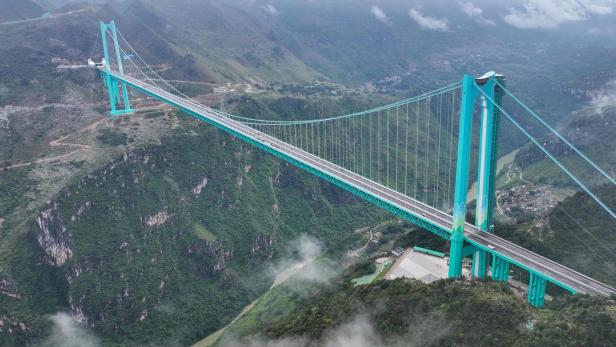 Die Huajiang Grand Canyon Bridge überspannt ein grünes Tal mit Bergen im Hintergrund.
