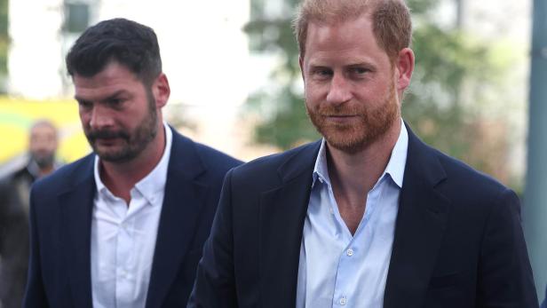 Prinz Harry in blauem Anzug, begleitet von einem Mann mit Bart.