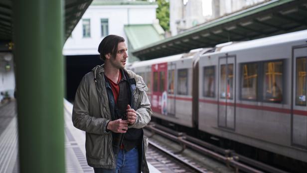 Ein Mann mit langer Jacke steht an einem Bahnsteig neben einer einfahrenden U-Bahn.