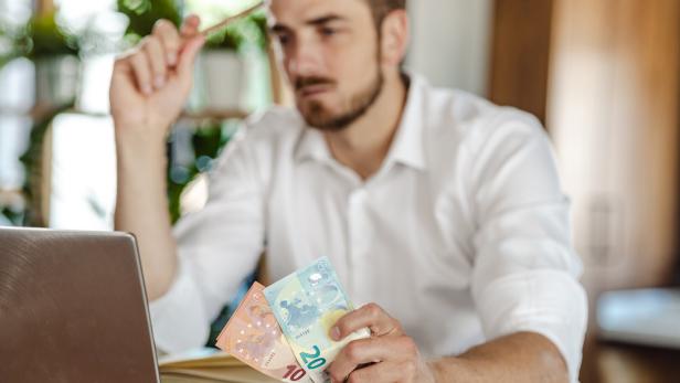 Mann mit Geld in der Hand sitzt vor einem Laptop