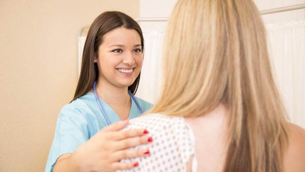 Frau in Krankenhauskleidung mit lächelnder Ärztin.
