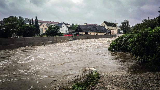 Der Fluss vor Gmünd ist aufgrund von Starkregen über die Ufer getreten und schabt gegen den errichteten Hochwasserschutz. Im Hintergrund ist die Stadt zu sehen.