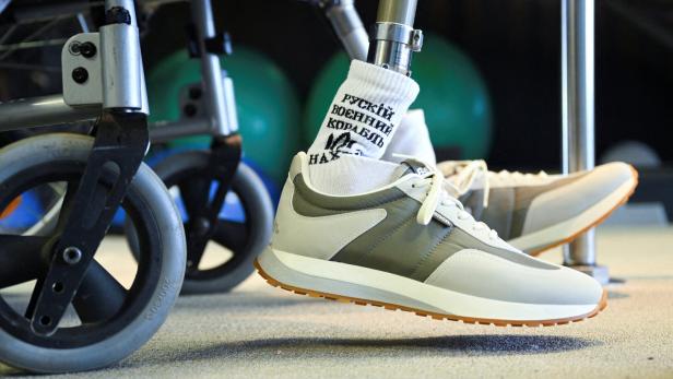 Zwei Beinprothesen in Sportschuhen neben einem Rollstuhl.