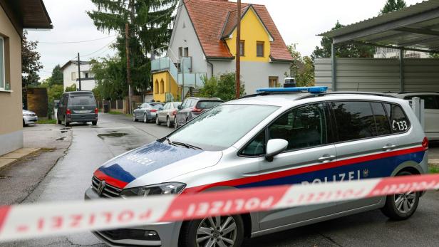 Absperrband der Polizei vor Polizeiauto, dahinter Häuser