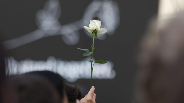 Eine Hand hält eine einzelne weiße Rose vor einem dunklen Hintergrund mit einer verschwommenen grafischen Darstellung einer Blume.