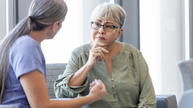 Zwei Frauen sitzen zusammen, eine hört nachdenklich zu, während die andere etwas erklärt.