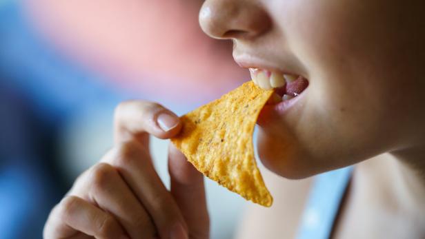 Unrecognizable happy teenage girl biting spicy nacho chip at home