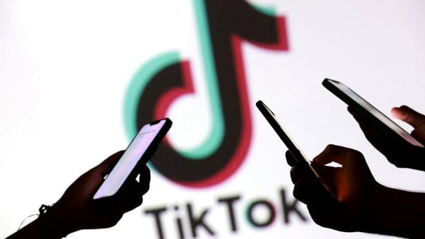 FILE PHOTO: Illustration shows teenagers pose for a photo while holding smartphones in front of a TikTok logo