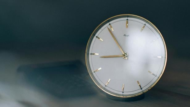 Analoge Uhr mit goldenen Zeigern und Rand auf einem Holztisch.