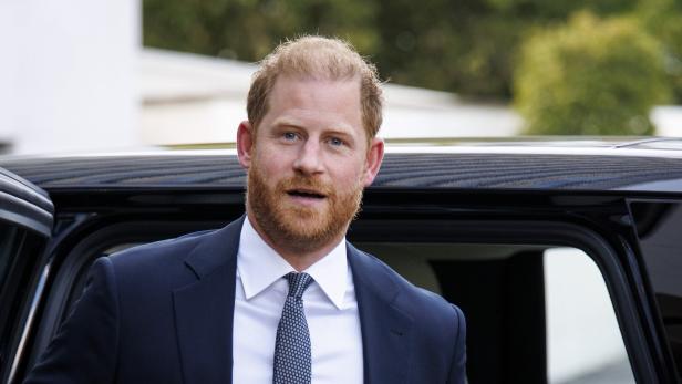 Prinz Harry, im dunklen Anzug und mit Krawatte, steht vor einem schwarzen Auto.