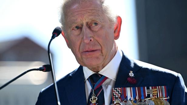 König Charles III. spricht am Mikrofon und trägt einen dunklen Anzug mit Orden.