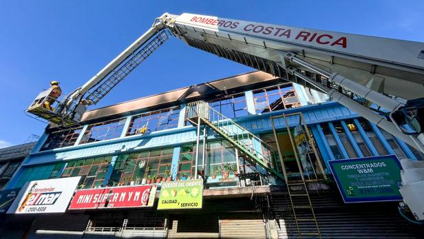 Ein Feuerwehrkran mit Feuerwehrleuten löscht einen Brand im oberen Stockwerk eines Geschäftsgebäudes.