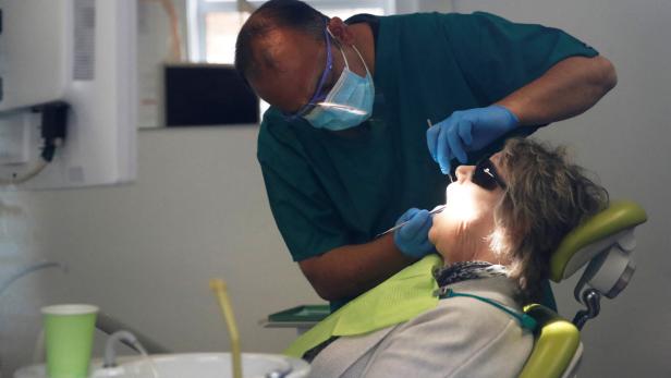 Ein Zahnarzt untersucht den geöffneten Mund einer älteren Patientin auf einem Behandlungsstuhl.