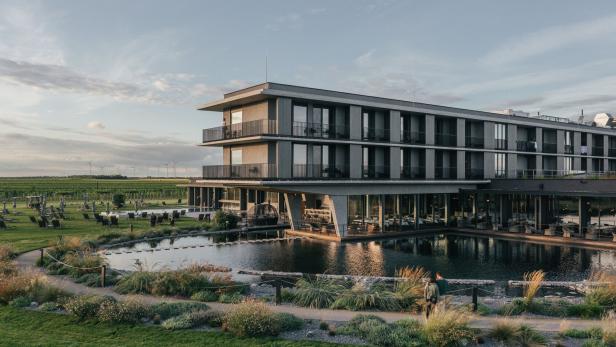 Ein modernes Hotel mit Pool liegt inmitten einer grünen Landschaft mit Weinbergen.