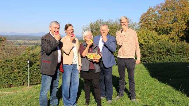 Fünf Personen stehen im Freien und essen Äpfel, eine Frau hält einen Korb voller Äpfel.