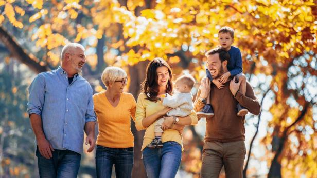 Eine Familie spaziert im Park, umgeben von bunten Herbstblättern und sonnigem Wetter.