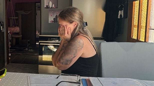 Eine Frau mit Tätowierung sitzt verzweifelt an einem Tisch mit Dokumenten.