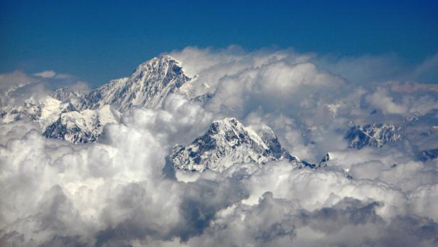 Verschneite Berggipfel ragen über dichte Wolken in einen klaren, blauen Himmel.