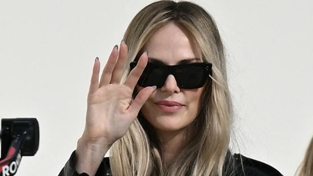 Charlize Theron mit Sonnenbrille und Lederjacke hält die Hand vor das Gesicht.