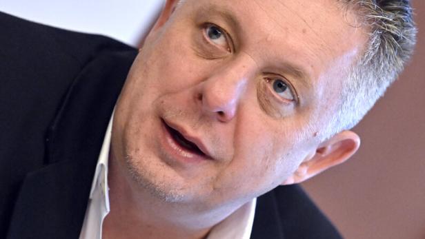 Ein Mann mit Anzug und offenem Hemd gestikuliert mit der Hand.