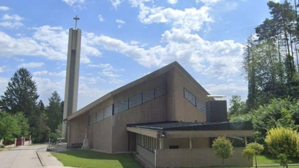 Eine moderne Kirche mit einem hohen Turm und einem Kreuz darauf ist von Bäumen umgeben.