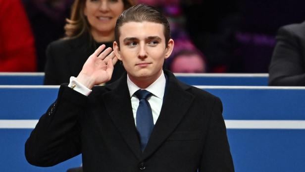 Barron Trump im dunklen Mantel hält die Hand an sein Ohr.
