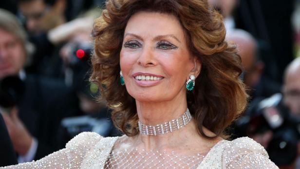 Sophia Loren lächelt mit auffälligem Schmuck vor einem unscharfen Hintergrund.