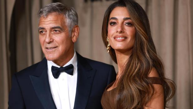 George und Amal Clooney posieren lächelnd vor einem Hintergrund mit der Aufschrift "For Justice".