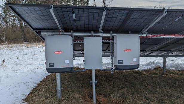 Zwei Solarpanels auf einem schneebedeckten Feld, umgeben von einer winterlichen Landschaft.