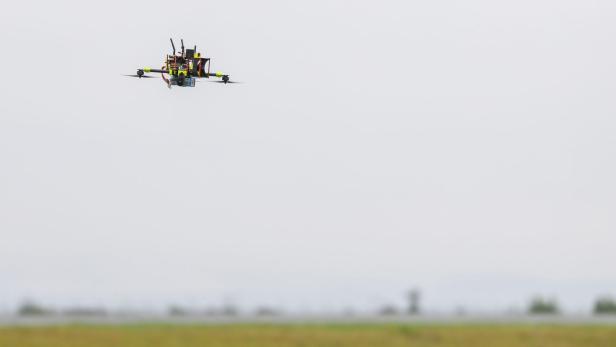 Forscher entwickeln Drohnenabwehr in Cochstedt Eine Drohne mit sichtbaren elektronischen Komponenten fliegt über ein offenes Feld bei bewölktem Himmel.